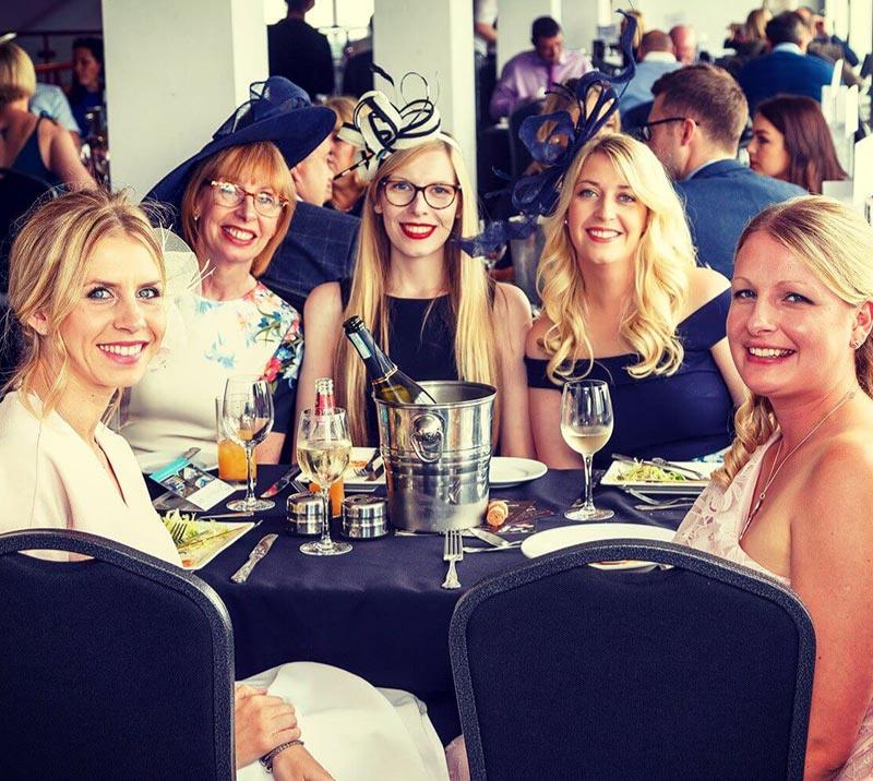 Group of dressed up ladies sitting at a restaurant table, smiling for a photo.