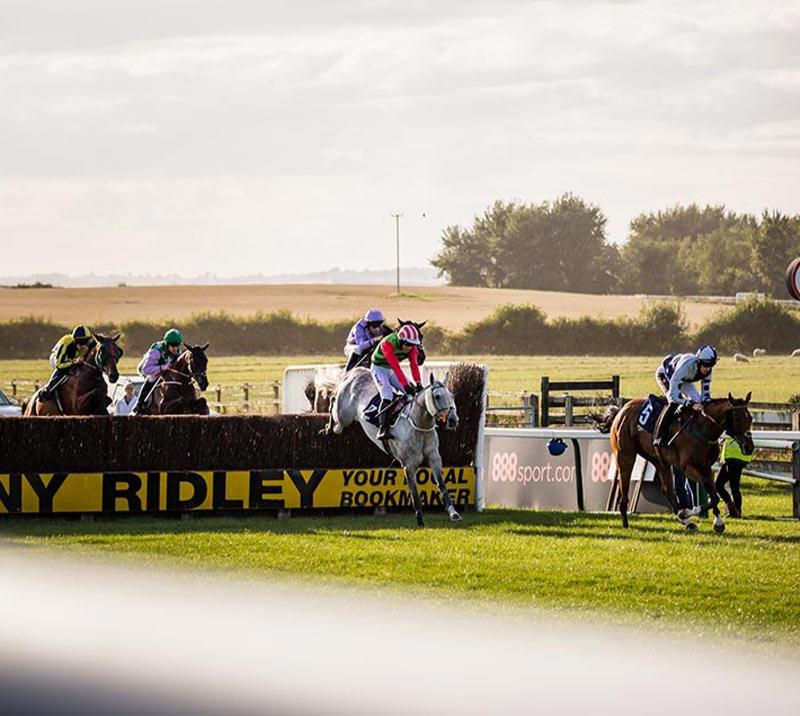 Jockeys jumping over a hurdle during a race at Sedgefield Racecourse.