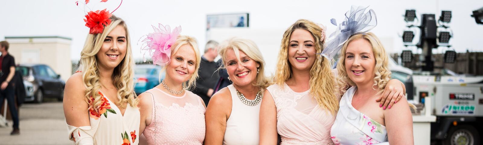 A group of ladies dressed in pink for the races posing for a picture.