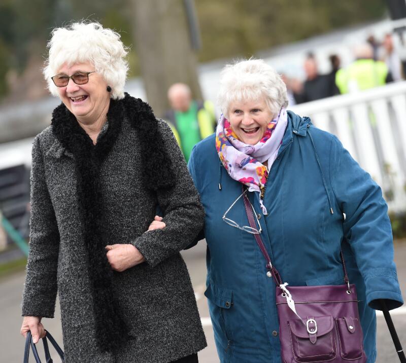 Two older race goers wrapped up for the weather smiling as they walk into the racecourse